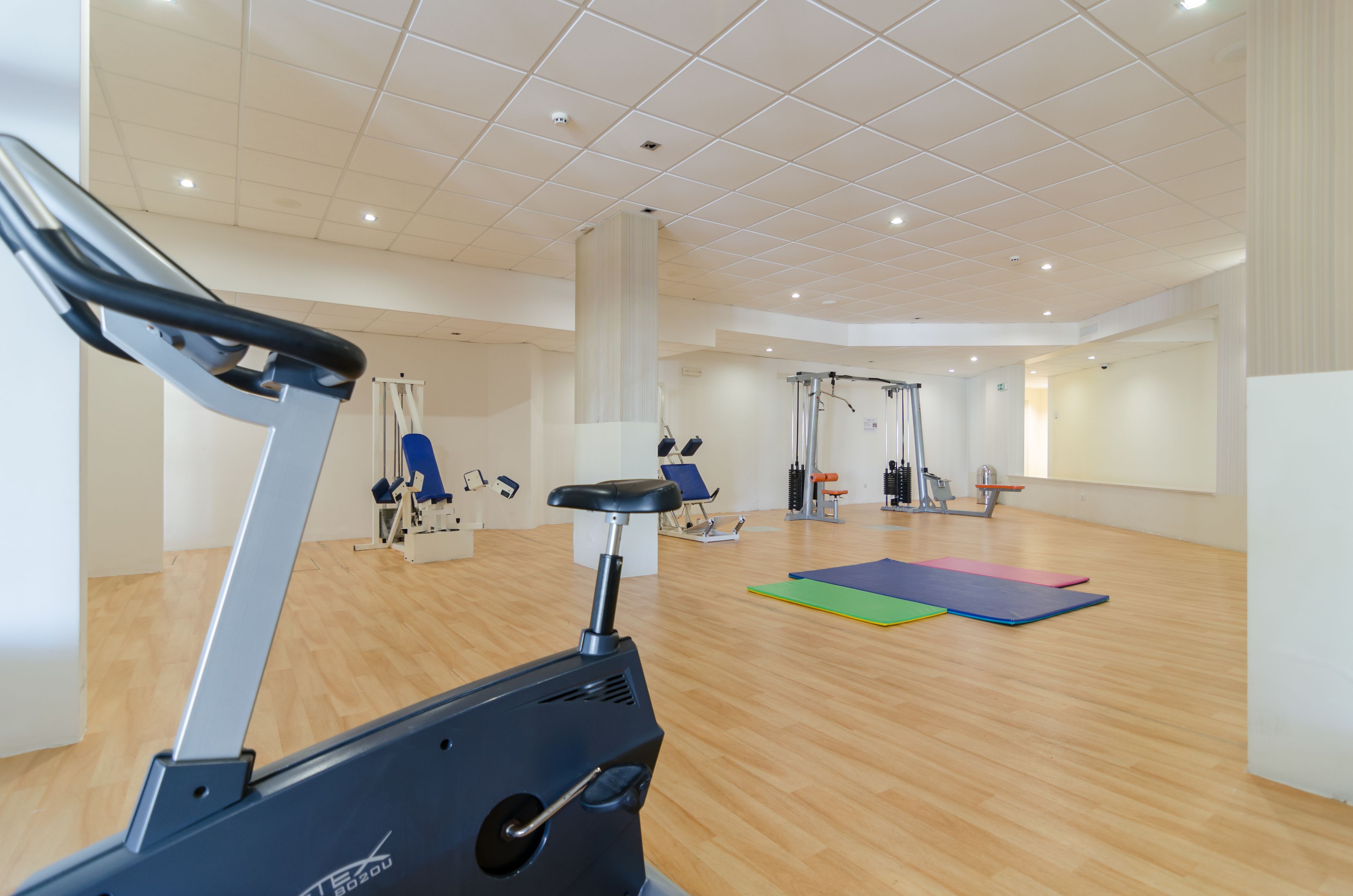 Une salle de sport spacieuse équipée de machines de cardio, d’appareils de musculation et de tapis au sol.