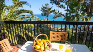 Un balcon avec un panier en osier rempli de fruits, un verre de jus et une carafe posée sur une table.