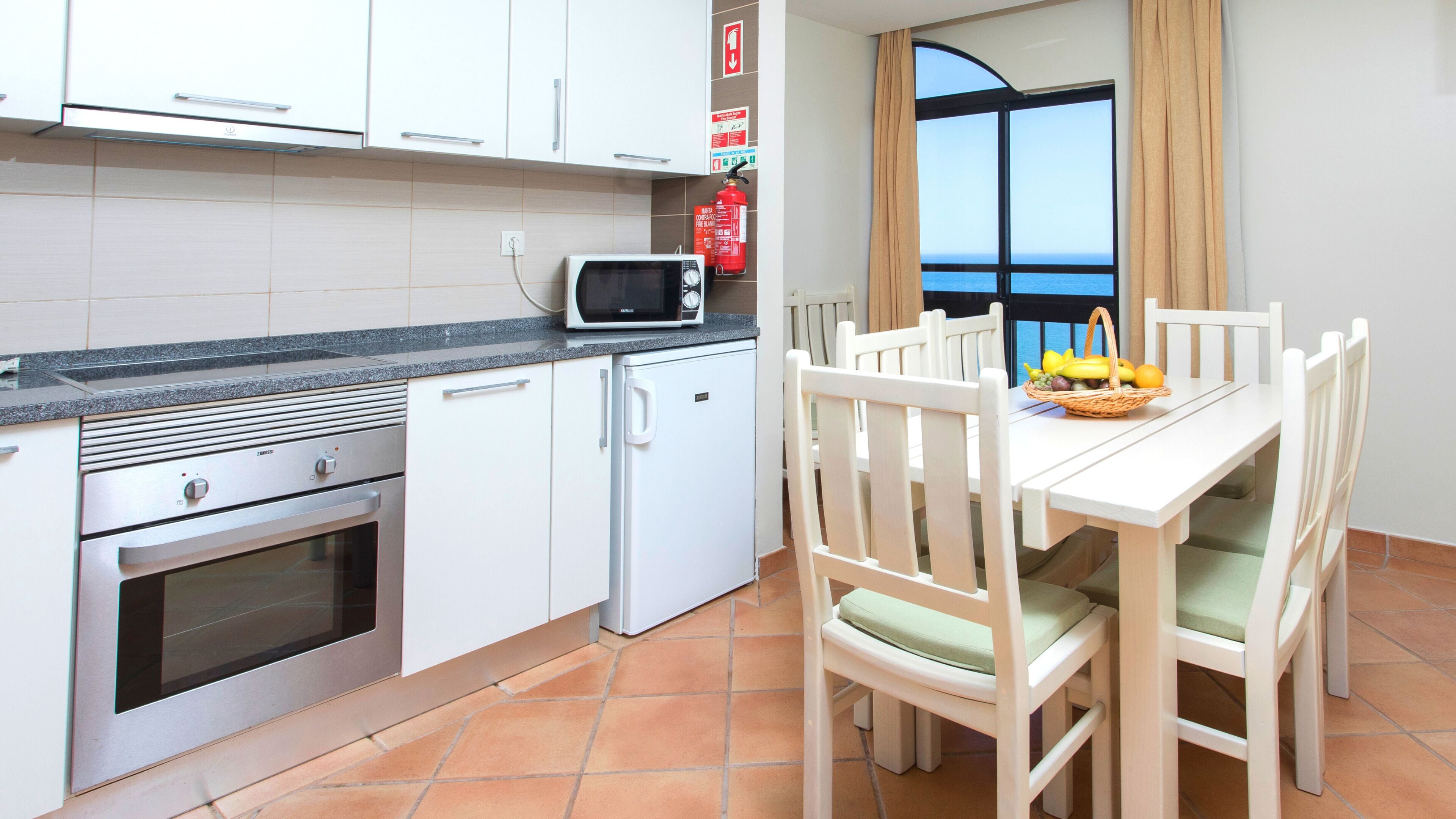 A compact kitchen with white cabinets, a microwave, a small refrigerator, and a dining area with a table and chairs.