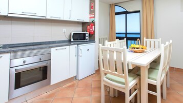 Cocina compacta con armarios blancos, microondas, refrigerador pequeño y zona de comedor con mesa y sillas.