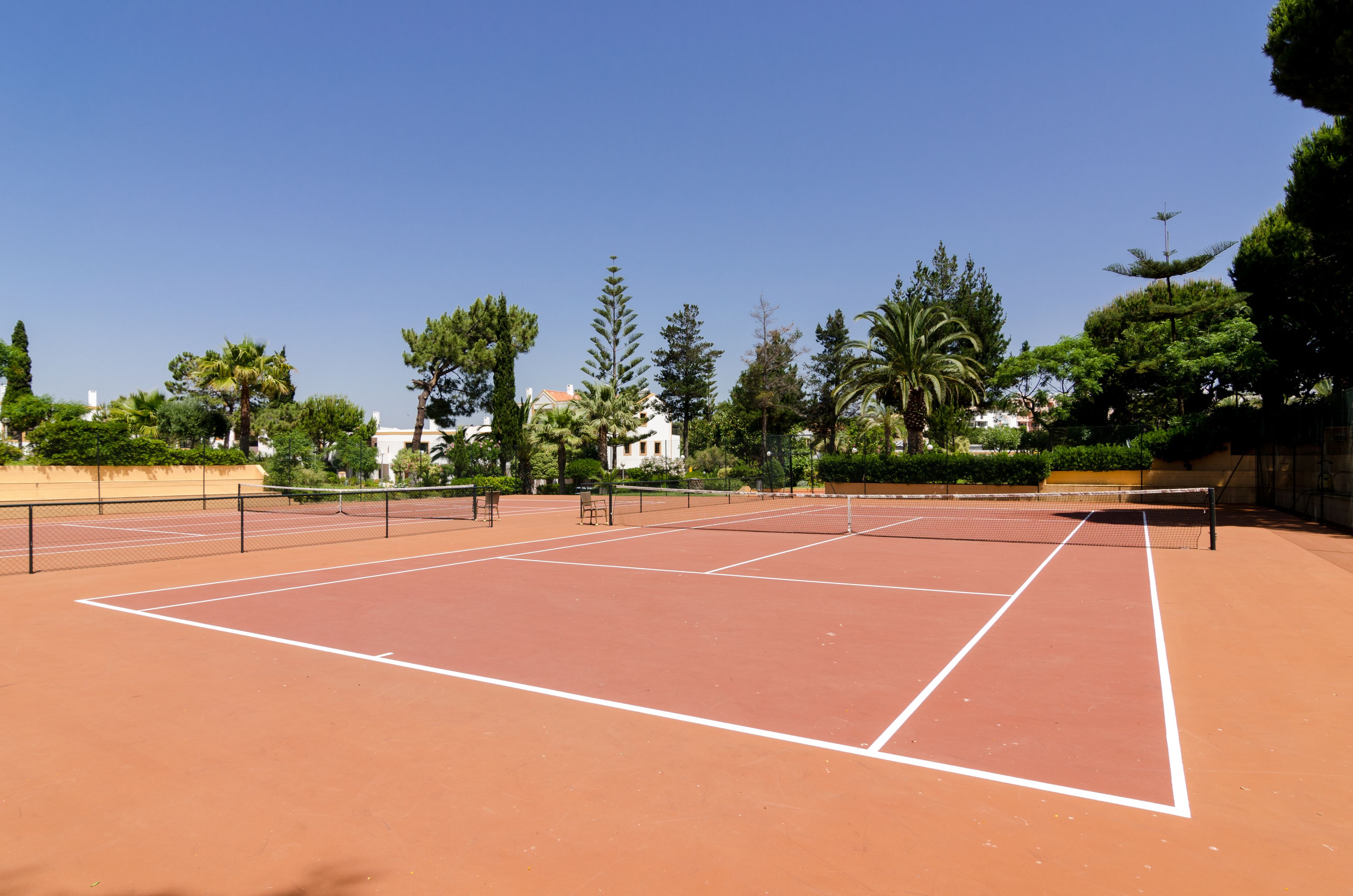 Una cancha de tenis con red, rodeada de árboles y edificios.