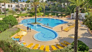 Un espace piscine d’un complexe hôtelier comprenant plusieurs piscines, des chaises longues et des palmiers.