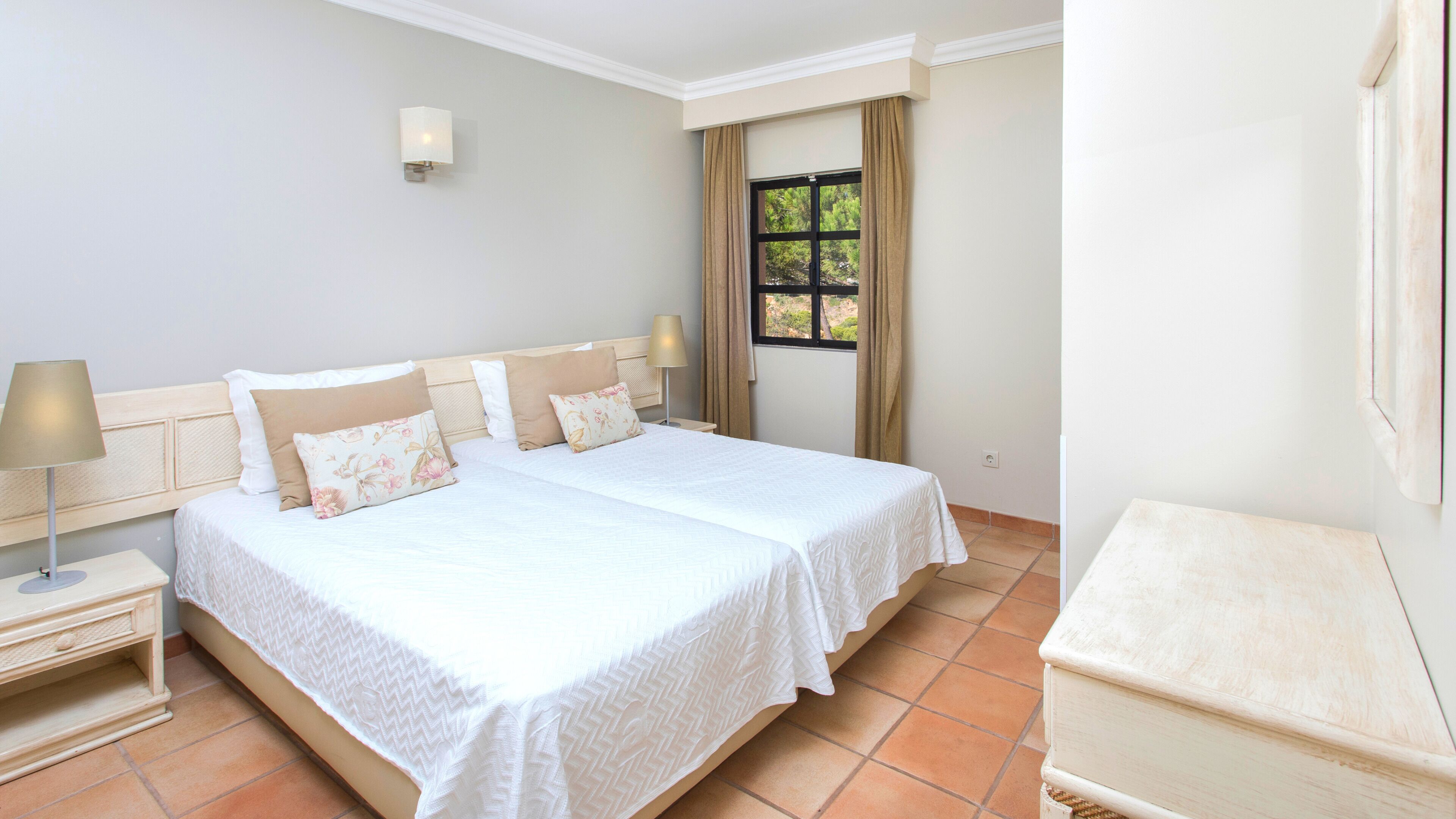 A double bed with a white bedspread and two nightstands with lamps.
