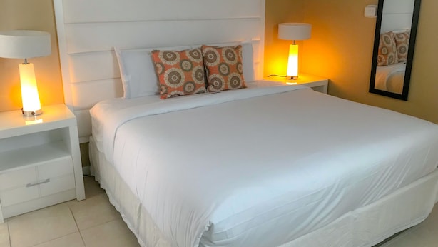 Hotellihuone, jossa on suuri sänky, kaksi yöpöytää valaisimineen, sängynpääty ja peili seinällä.