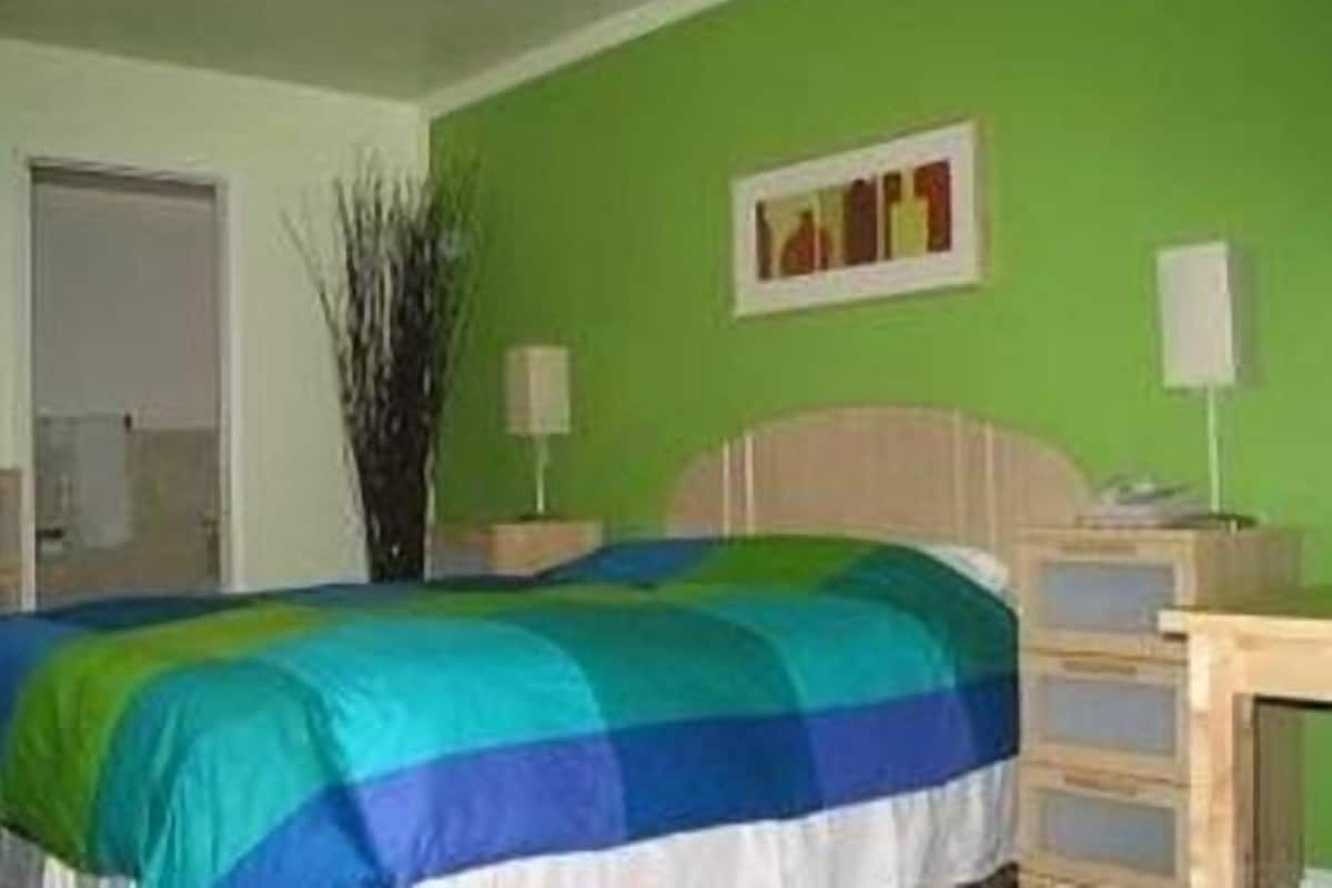 A bedroom with a bed, a nightstand, a lamp, a wall-mounted picture, and a door.