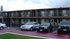 A building with multiple parking spaces and a red parking lot. - Sequoia Inn (Redwood City)