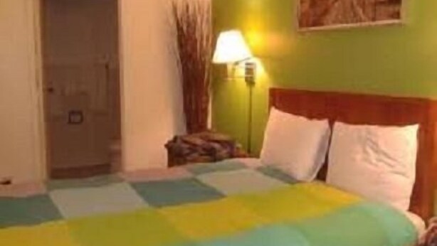A hotel room with a bed, a nightstand, a lamp, and a door. - Sequoia Inn (Redwood City)