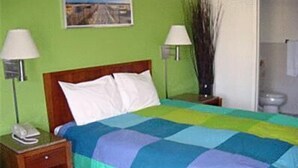 A bed with a multicolored quilt, two bedside lamps, a nightstand with a phone, and a picture on the wall. - Sequoia Inn (Redwood City)