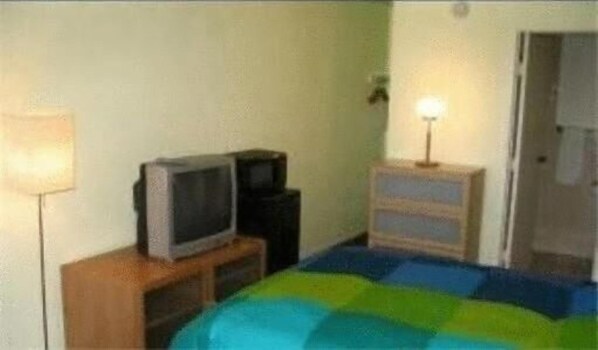 A room with a bed, a television on a wooden stand, a dresser, and a lamp.
