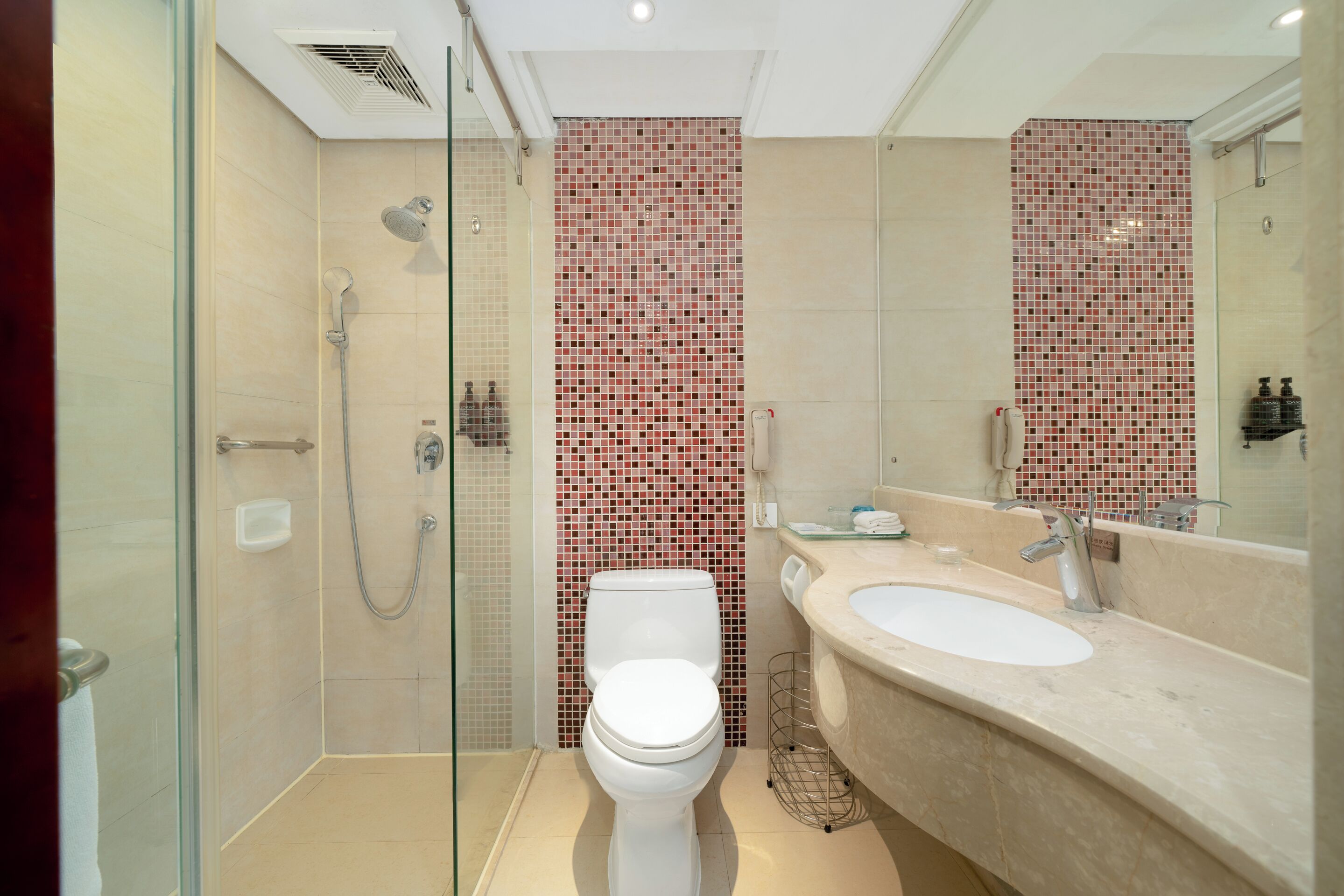 A modern bathroom with a glass-enclosed shower, a white toilet, and a beige sink with a large mirror.