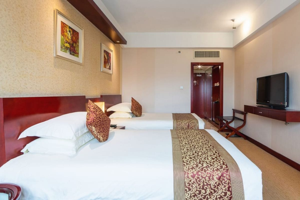 Ein Hotelzimmer mit zwei Betten, einem Fernseher und einer Tür zu einem Badezimmer.