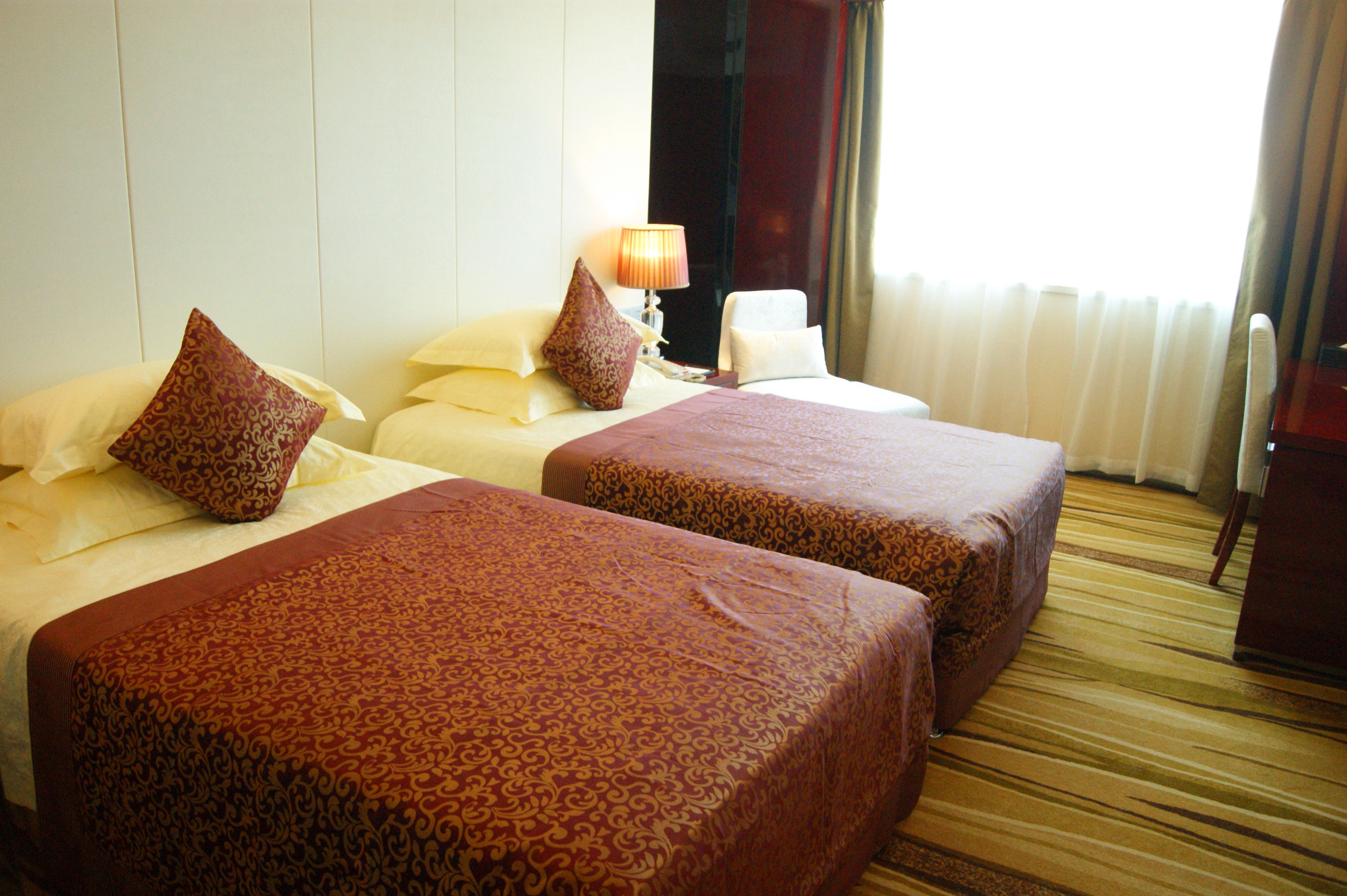 A hotel room with two beds, each with patterned bedspreads, a bedside lamp, and a window with curtains.