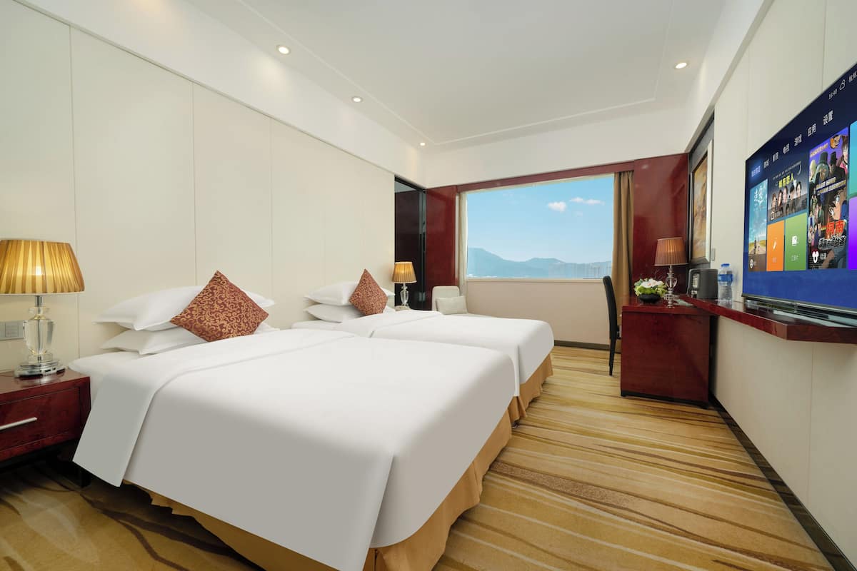 Ein Hotelzimmer mit zwei Betten, einem Schreibtisch, einem Fernseher und Bergblick.