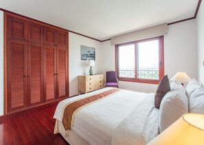 Un dormitorio con una cama grande, armario de madera, una silla, cómoda y una ventana con vistas.