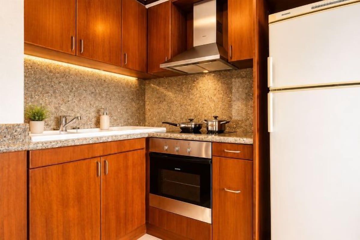Una cocina con armarios de madera, horno de acero inoxidable, refrigerador blanco, encimeras de granito y salpicadero de granito.