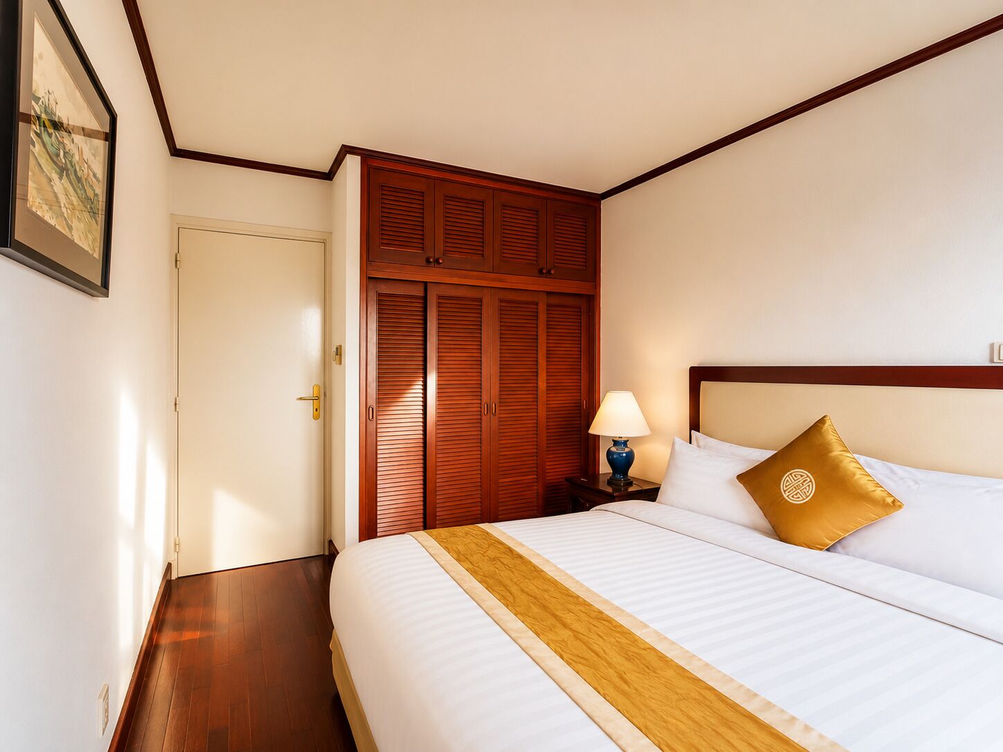 Une chambre d’hôtel avec un lit, une armoire en bois, une table de chevet, une lampe et un tableau encadré au mur.