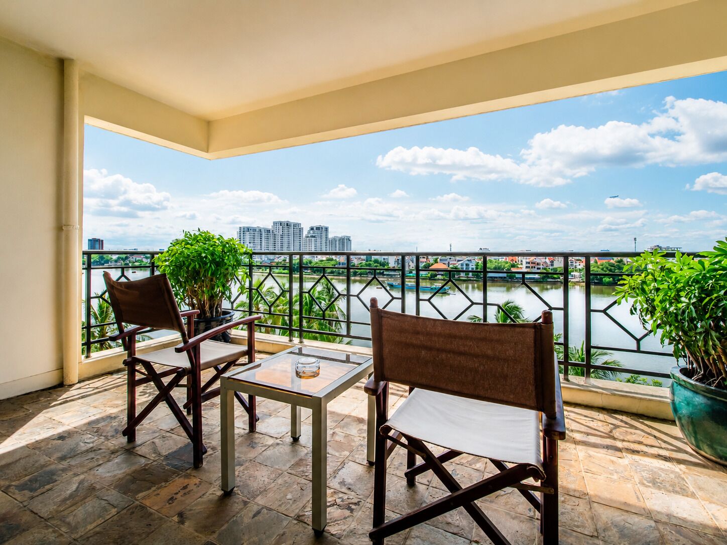 Ein Balkon mit zwei Stühlen und einem Tisch, mit Blick auf einen Fluss und Gebäude in der Ferne.