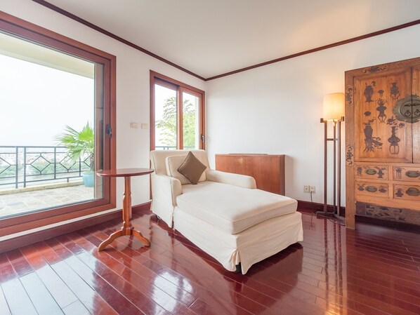 Un dormitorio con cama, una mesita, un aparador de madera con detalles decorativos y vistas a un balcón con plantas.