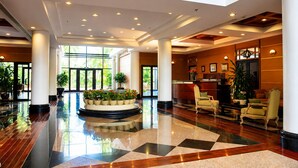 A spacious lobby with a checkered floor, a central planter with plants, and a reception desk.