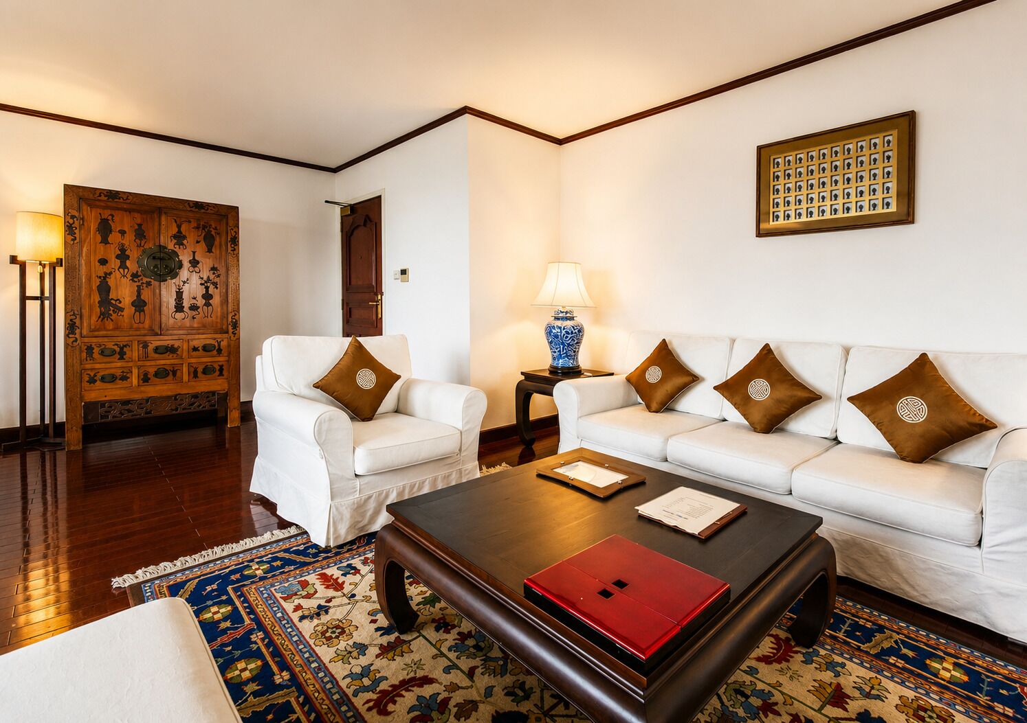 A room with a white sofa, a wooden coffee table, a patterned rug, a lamp, and a decorative panel on the wall.