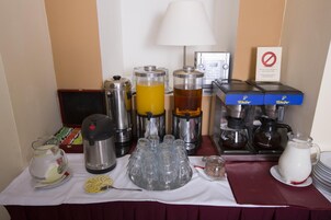 Disposição de buffet de café da manhã com diversos dispensadores de alimentos e bebidas, incluindo máquina de café e dispensador de leite.