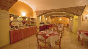 A dining area with multiple tables and chairs, a buffet setup, and brick arches. - Hotel Tyl (Prague)