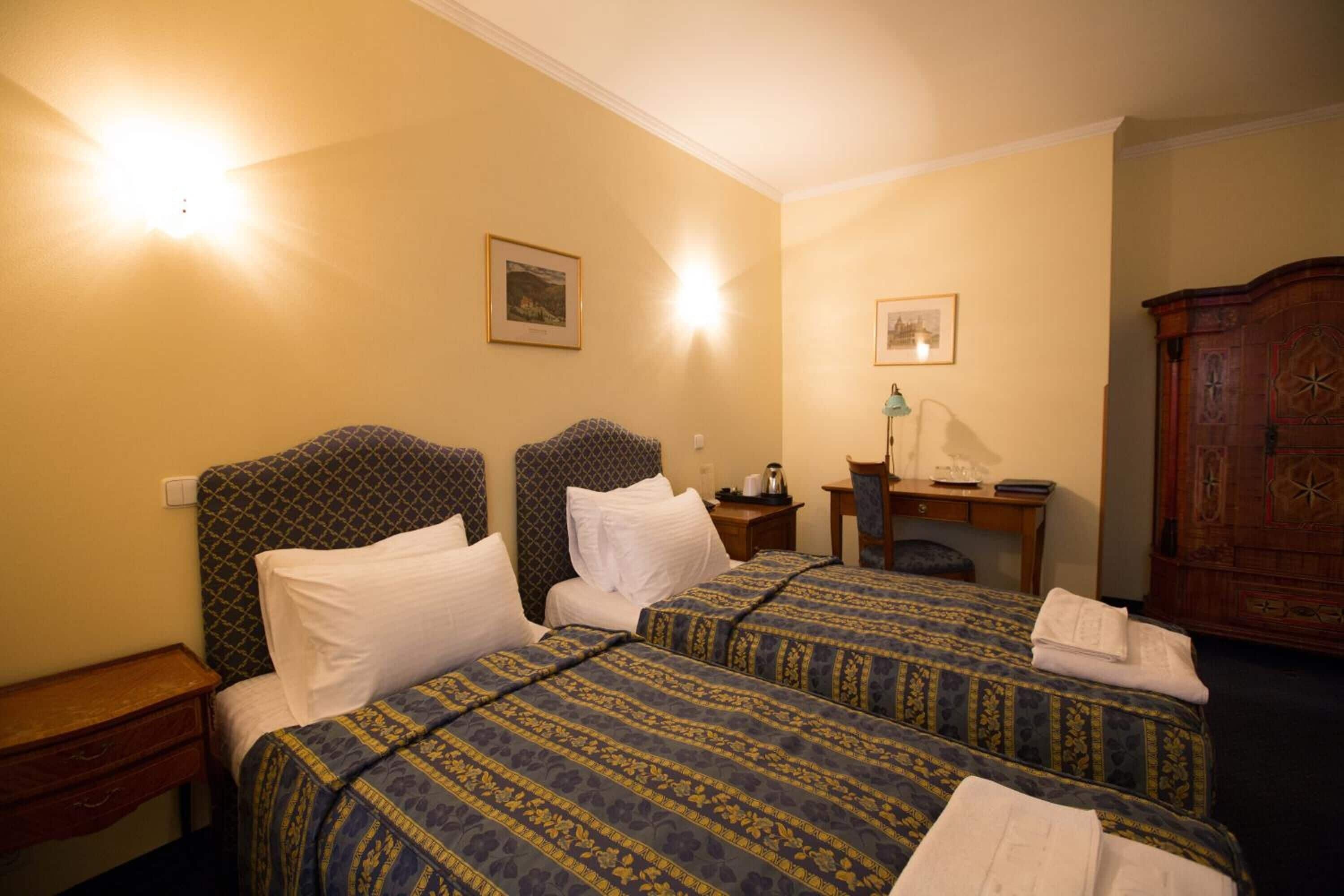 A hotel room with two beds, a desk, a chair, and a wooden cabinet.
