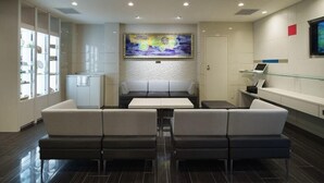 Un área de recepción moderna con zona de estar, mostrador de recepción y un cuadro abstracto grande en la pared.