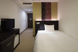 A hotel room with a bed, a TV on a desk, and a wall with a floral pattern.