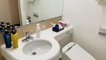 Un baño con lavamanos blanco, un espejo, inodoro y artículos de aseo en la encimera.