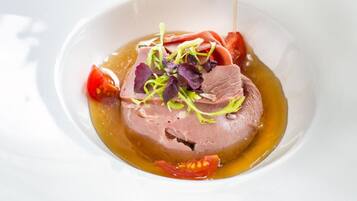 Un plato blanco con un guiso de carne, adornado con vegetales verdes y salsa vertiéndose sobre él.