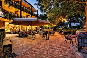 Un patio al aire libre con mesas y sillas, una zona de estar techada y luces colgantes.