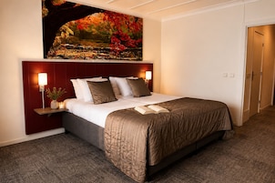 Habitación de hotel con cama, lámparas de noche, mesita de noche, un cuadro y una puerta.