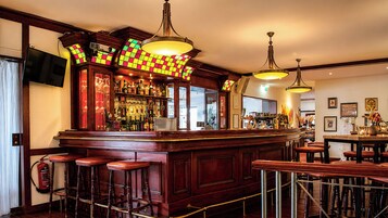 A bar area with wooden bar stools, a counter with a glass display, and hanging pendant lights.