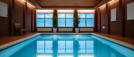 A swimming pool with a wooden ceiling and brick walls, large windows with a view of the sky, and potted plants.