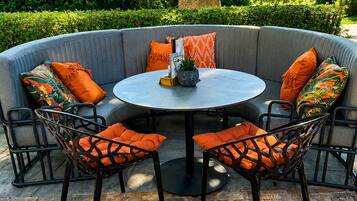 Een rond zitgedeelte buiten met een tafel, gestoffeerde stoelen en diverse kussens.