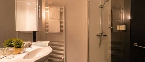 Un baño moderno con ducha envuelta en vidrio, tocador con lavabo y espejo.
