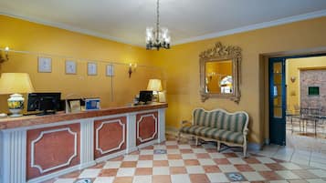 A reception area with a marble counter, a chandelier, framed pictures, a sofa, and a mirror.