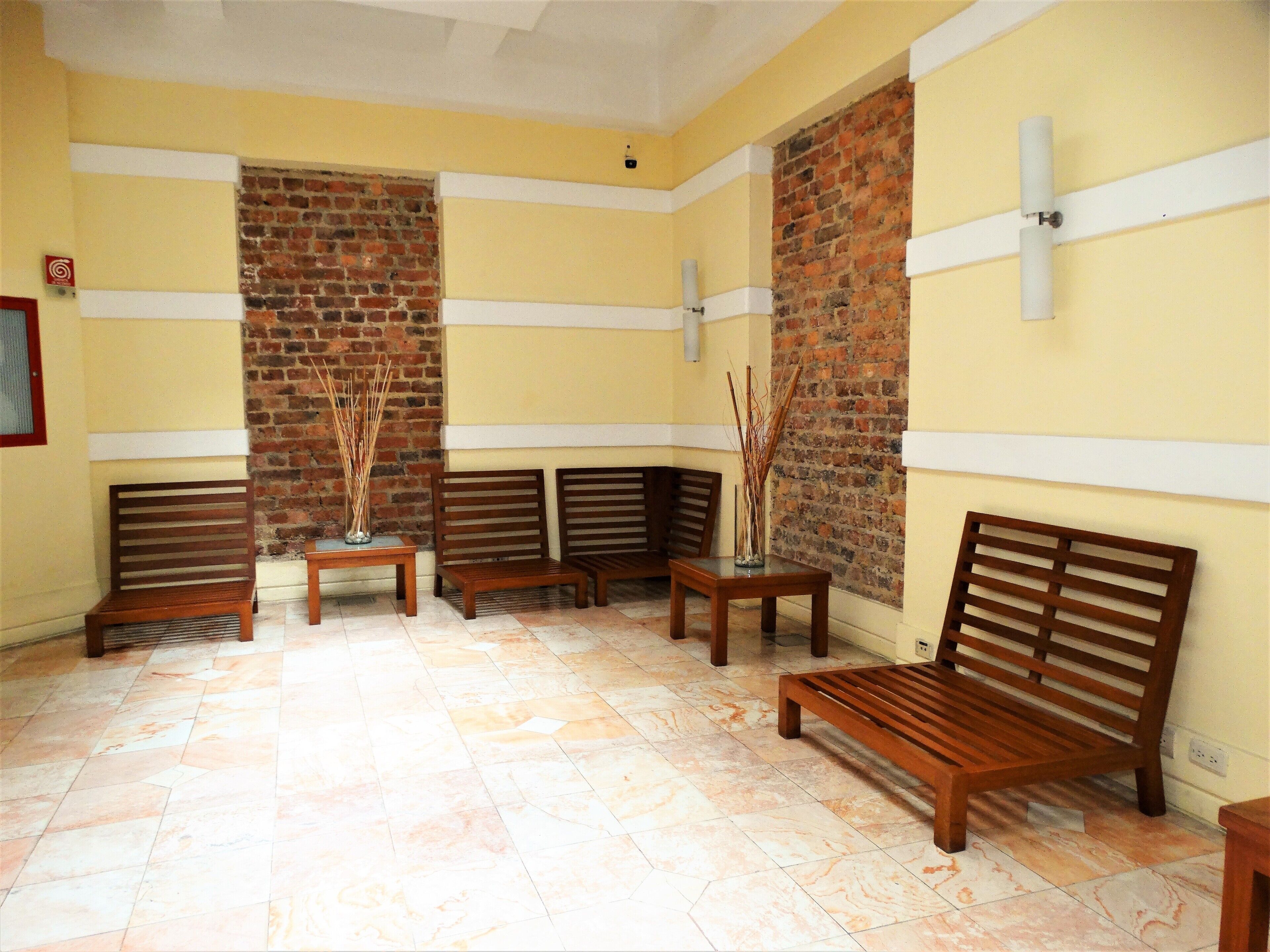 A room with a tiled floor, wooden benches, and a brick wall.