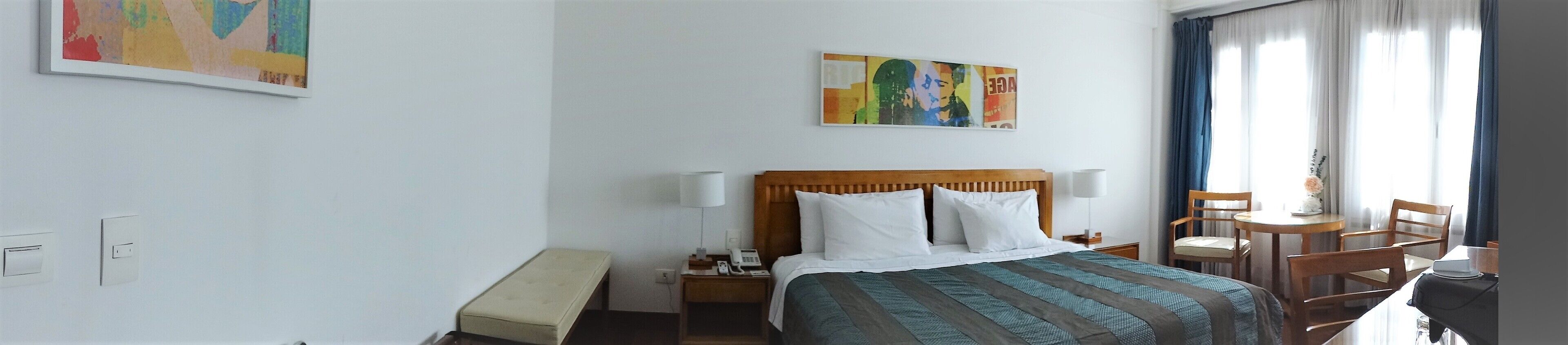Een hotelkamer met een bed, nachtkastje, lamp, stoel en een tafeltje met een vaas.