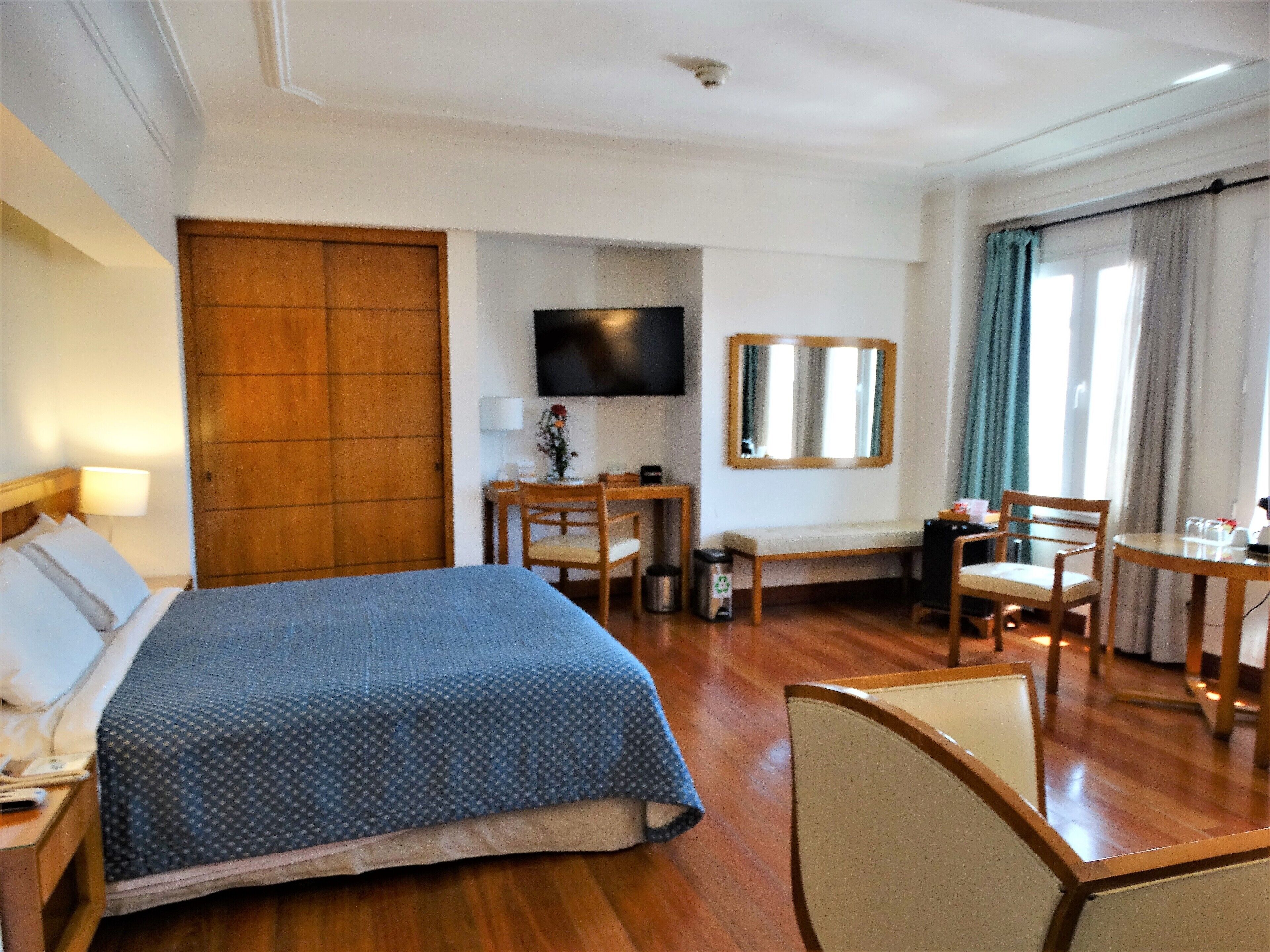 A hotel room with a bed, a desk, a chair, a television, and a window with curtains.