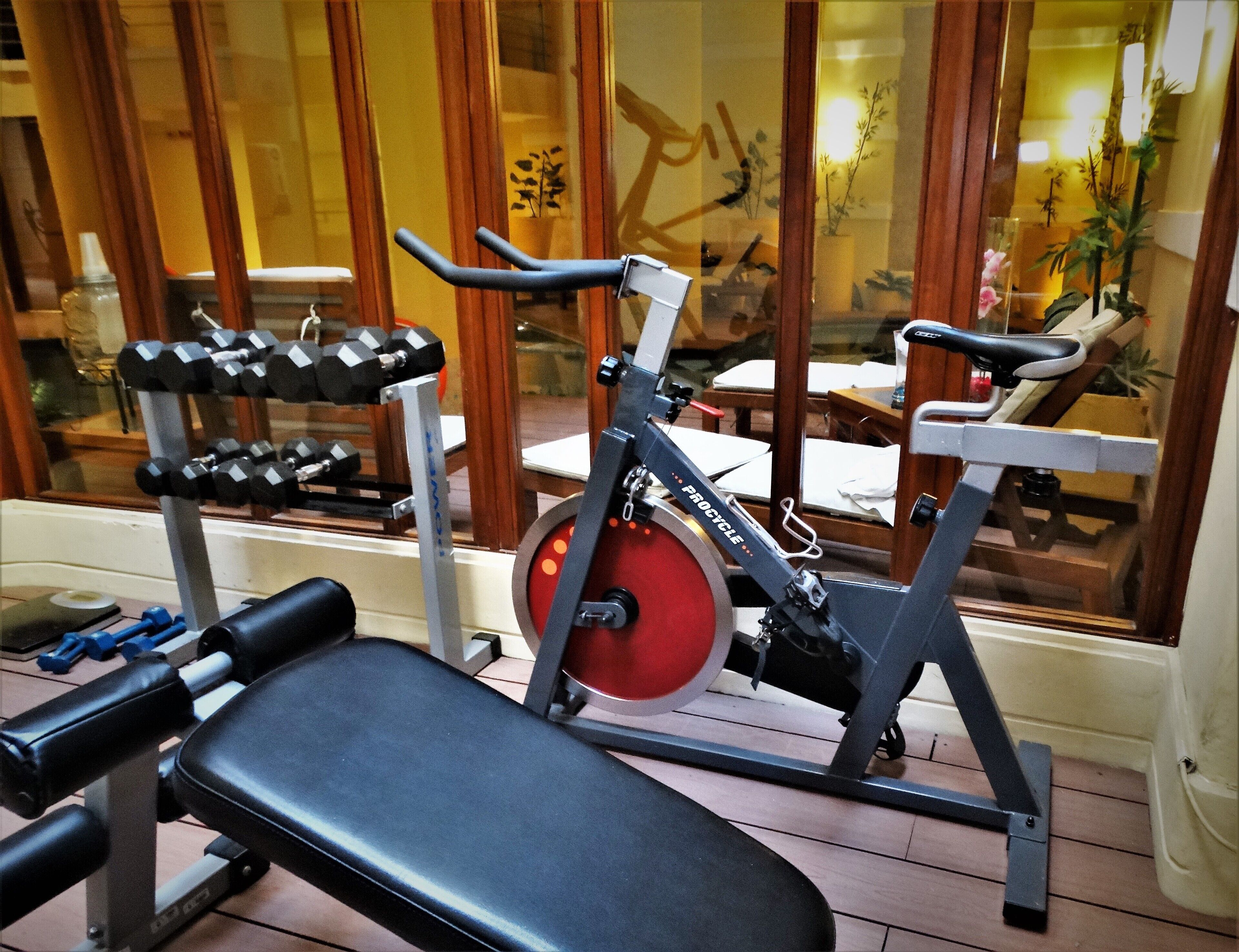 Een huisgym met een bankdrukapparaat, gewichten en een hometrainer.