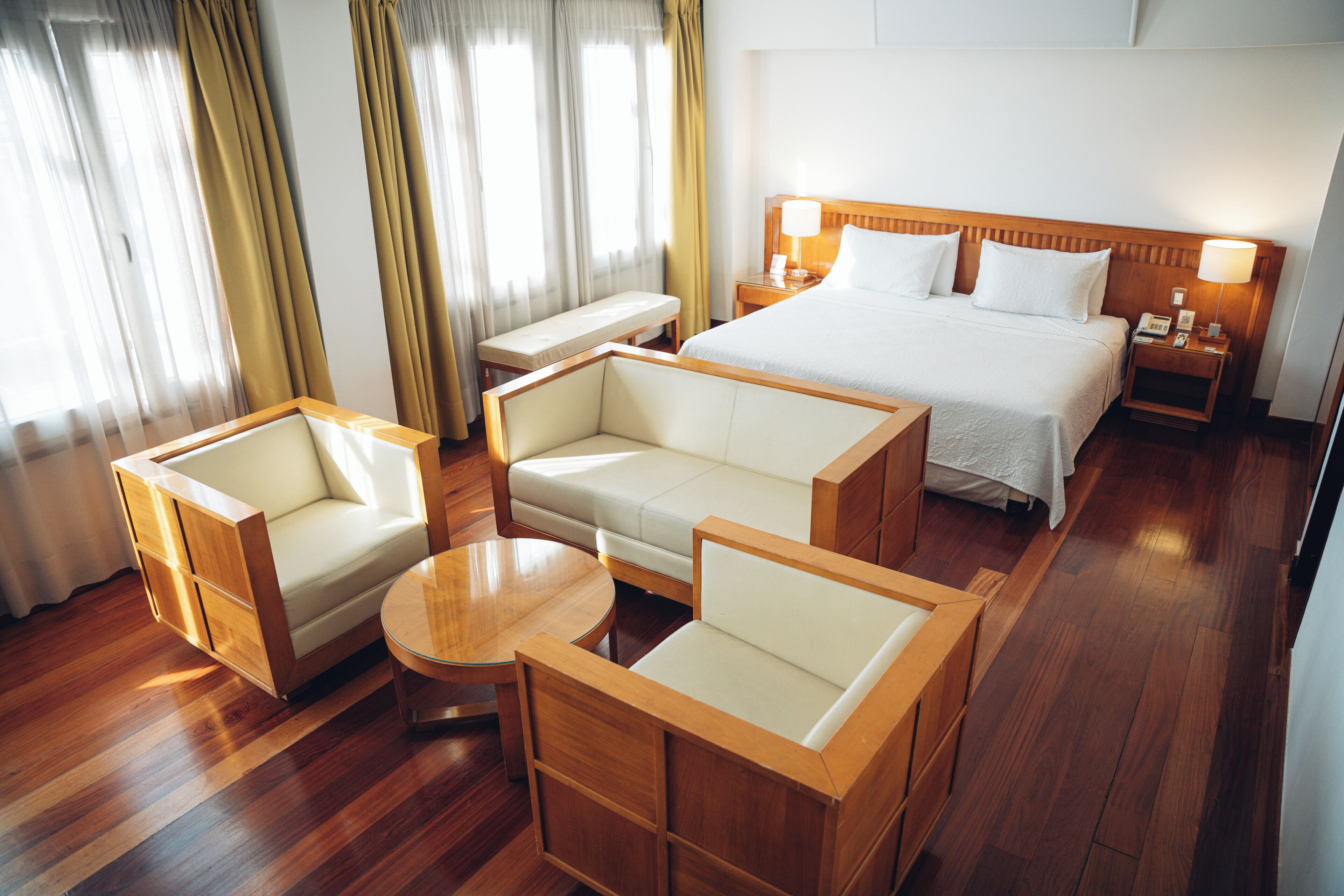 A hotel room with a large bed, two sofas, a small table, and a bench.