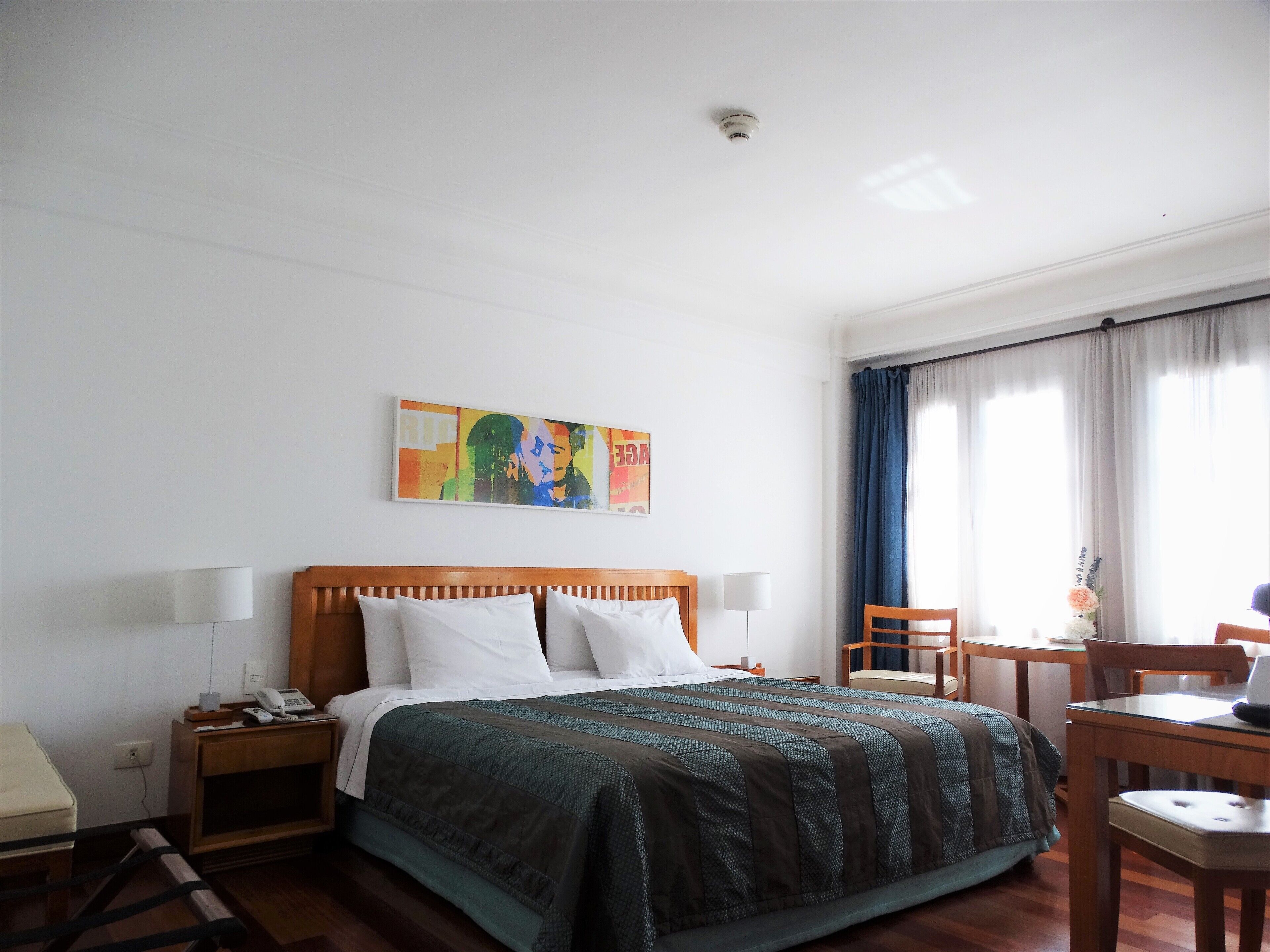 Una habitación de hotel con una cama de madera, un escritorio, una silla, un teléfono y un cuadro en la pared.
