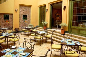 An outdoor dining area with multiple tables and chairs, potted plants, and a brick wall. - Hotel de la Opera (Bogotá)