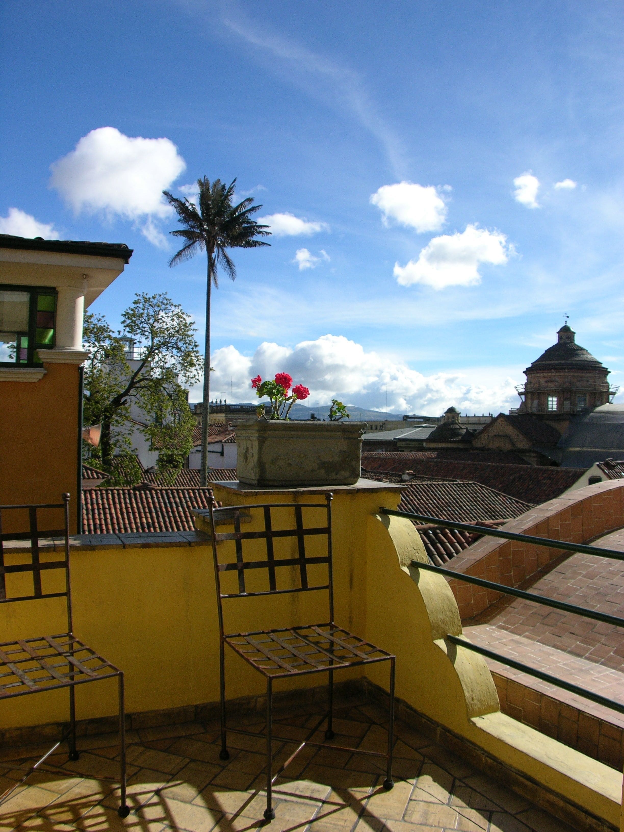 Una terraza en la azotea con una pared amarilla, una mesa de metal y una maceta.