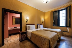 A hotel room with two beds, a bathroom with a mirror, and a window with blinds. - Hotel de la Opera (Bogotá)