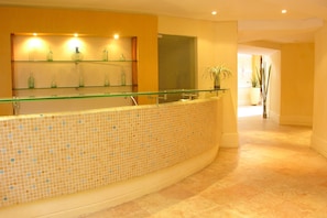 A reception area with a glass railing, tiled floor, and a plant in the background.