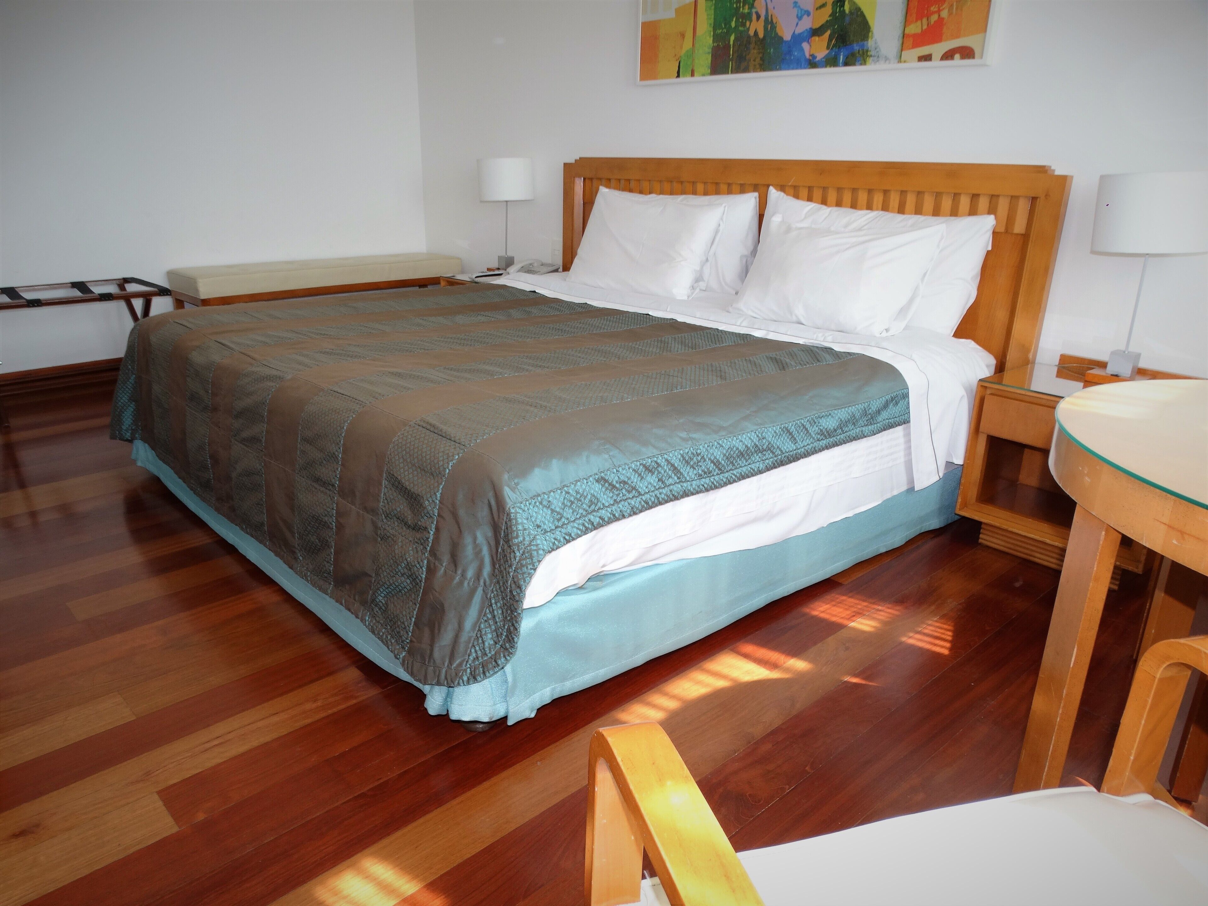 Un dormitorio ordenado con una cama de madera, una mesita de noche y una pequeña mesa redonda con superficie de vidrio.