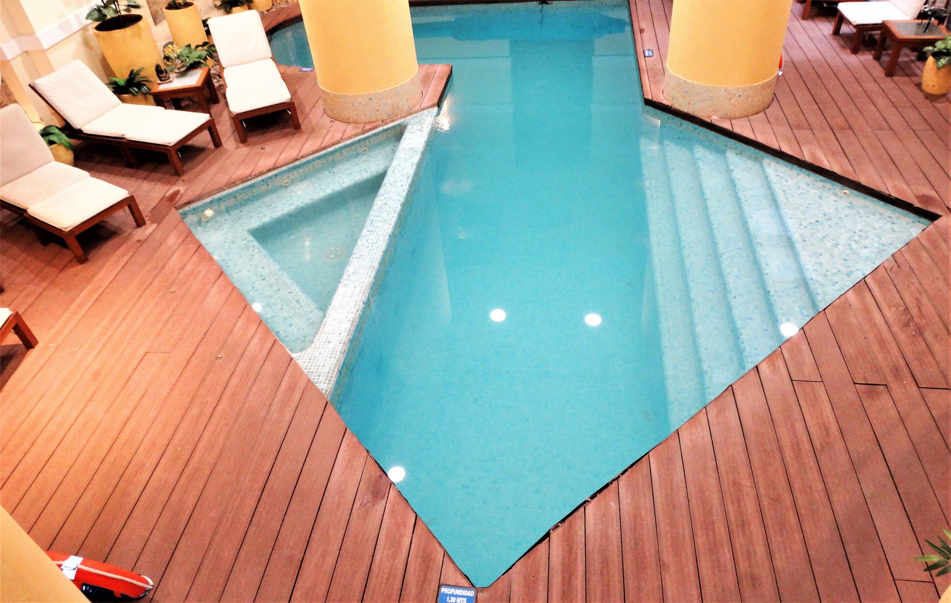 An indoor swimming pool with wooden flooring and lounge chairs.